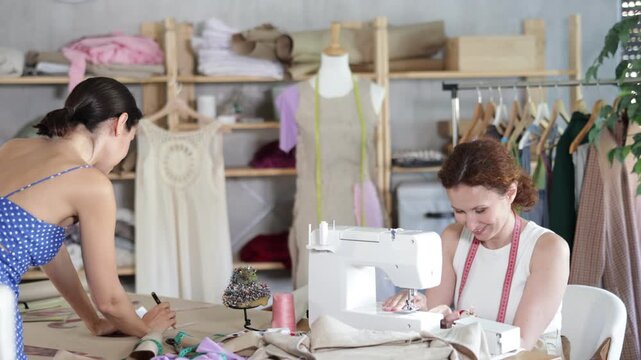 Woman tailor draw dress pattern with curve ruler on paper, female master seamstress sewing cloth with sewing machine. Tailor workplace with cut textile, sewing machine, thread, pins, needles, tape