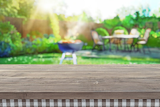 backyard with seating and lush greenery, patio area with green lawn and bbq grill blurred, wooden board