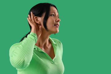 Fototapeta premium Young woman trying to hear something on green background, closeup