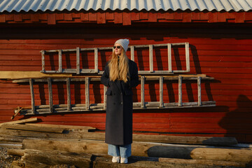 Obraz premium Young woman stands near wooden ladder in front of red barn during golden hour at rural location