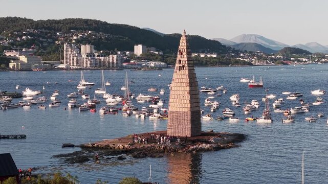 Alesund in Norwegen, Turm f&uuml;r Slinningsbalet. Sch&uuml;ler klettern auf Turm f&uuml;r die Sommersonnenwende. Umgeben von Schiffen bei sonnigem Wetter. Berge im Hintergrund. Pan Shot mit Drohne