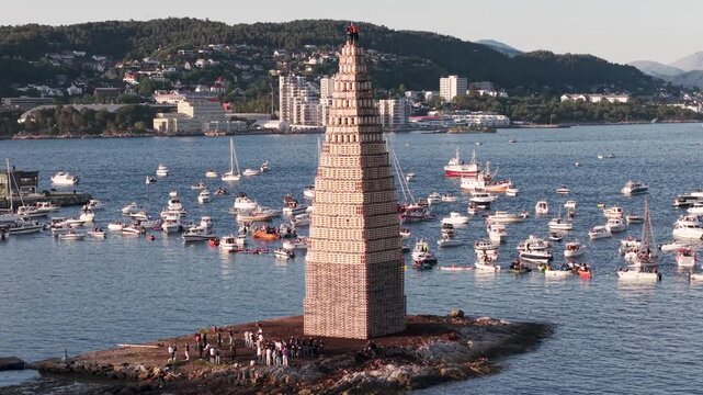 Alesund in Norwegen, Turm f&uuml;r Slinningsbalet. Sch&uuml;ler entz&uuml;nden Turm f&uuml;r die Sommersonnenwende. Umgeben von Schiffen bei sonnigem Wetter. Berge im Hintergrund. Pan Shot mit Drohne