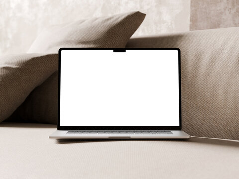 Silver laptop with an empty screen placed on a soft beige sofa with textured pillows.