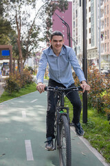 Naklejka premium A young man is standing next to his bike on a pathway in a city. He wears a light blue shirt and black pants.