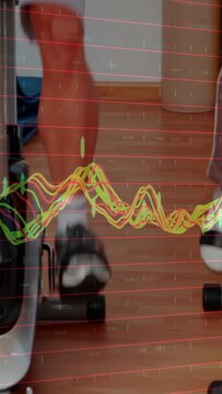 Vertical video: Graph scrolling, two adults pedaling bike, feet secured, tracking rehab progress