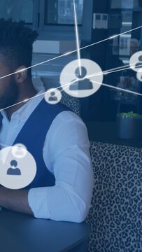 Vertical video: Man sitting booth touching laptop, causing network icons crossing face for business