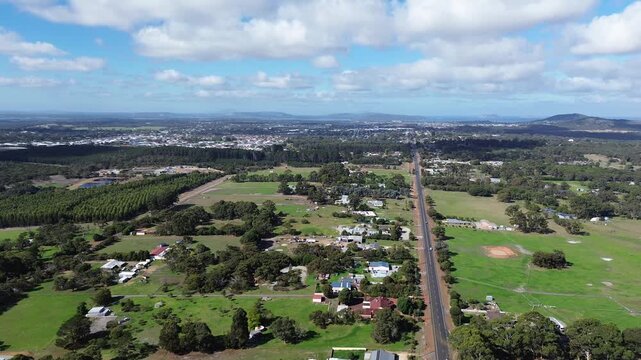 Aerial view of Albany Western Australia, view is looking over the countryside with the city and town in the background. Grass and agricultural feilds, blue cloudy sky with mountains in background