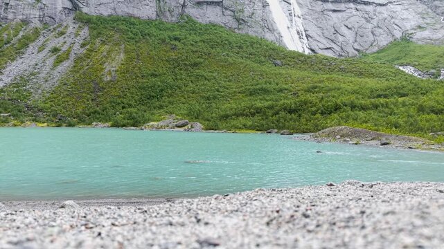 Aufnahme des Briksdalsbreen Gletschersees bei Regen. t&uuml;rkises Wasser flie&szlig;t in einen Bach mit B&auml;umen im Hintergrund. Raw unbearbeitet