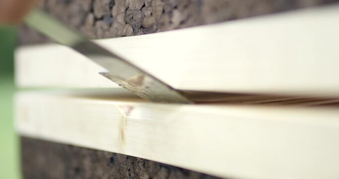 Close up of a metal hive tool prying open a modern wooden and cork beehive in an outdoor apiary