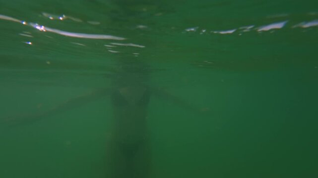 Woman swimming in sea captured half underwater and half above surface, slow motion movement, tropical ocean immersion and relaxed vacation mood