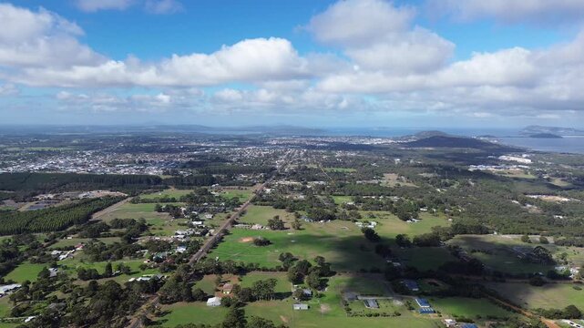 Aerial view of Albany Western Australia, view is looking over the countryside with the city and town in the background. Grass and agricultural feilds, blue cloudy sky with mountains in background