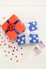 Obraz premium Gift boxes with USA flags and confetti on white wooden background. American Independence Day
