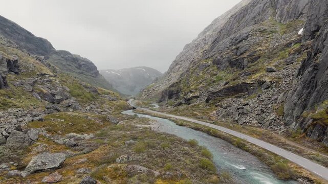 Drohnenflug &uuml;ber Fluss neben Stra&szlig;e in Skandinavien, umgeben von Bergen, mosige Landschaft bei nebligem Wetter. RAW unbearbeitet