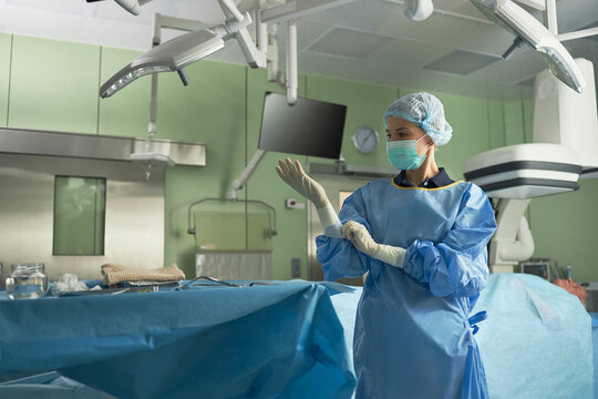 Caucasian young adult woman surgeon adjusting sterile gloves in operating room, preparing for procedure. Ideal for healthcare, surgery, hospital safety, medical team marketing
