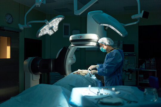 Wide shot of surgeon performing minimally invasive procedure in operating room under imaging equipment, representing modern healthcare technology. Ideal for medical services marketing