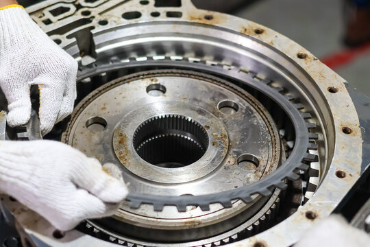 Mechanic hands in white gloves installing a steel clutch plate into a heavy duty automatic transmission assembly during a professional gearbox repair and maintenance service.
