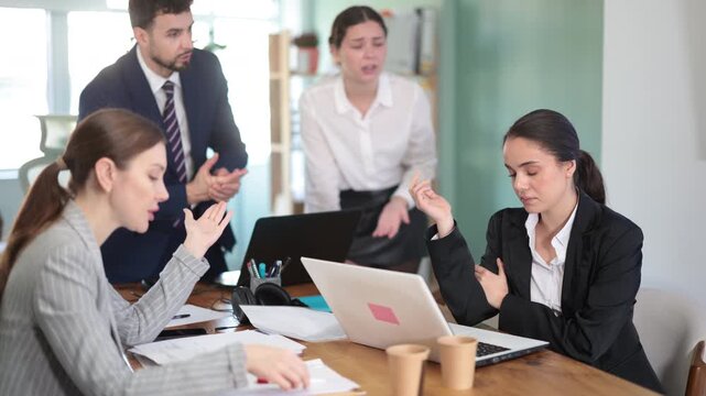 Group of women and man scold young woman while she sits looking sad in office