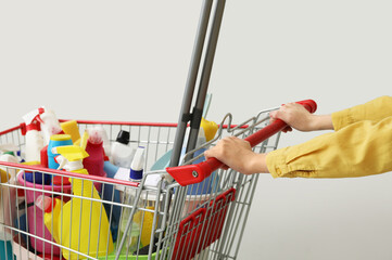 Woman with cleaning supplies in shopping cart on light background © Pixel-Shot