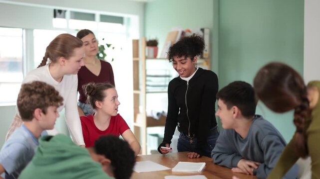 At round table meeting, teen participants discuss problem and try to find solution, teacher watching. Brain storm, team discussion, personal growth courses, psychological training, collegiate council 