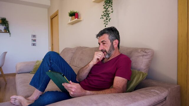 Middle aged bearded man using a tablet on a couch