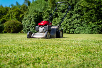 Obraz premium Petrol lawn mower on freshly cut green lawn. Professional landscaping equipment for garden maintenance, gasoline lawnmower on grassy field in well kept manor estate during sunny day