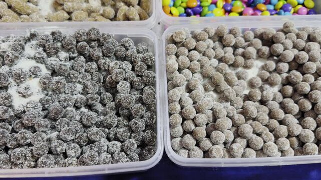 Tracking shot of assorted Indian churan goli in plastic containers, showing sugar coated digestive candies in varied textures and earthy tones arranged closely together!