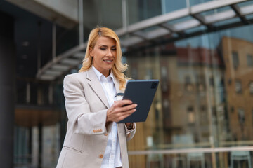 Fototapeta premium Businesswoman using tablet and drinking coffee outside office building