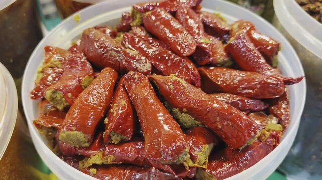 Camera orbiting closeup of stuffed red chilli pickle, showing glossy whole chilies filled with spiced masala and coated in rich oil, highlighting texture and vibrant color!