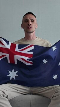 An Australian football fan watches football and cheers for his national team while holding an Australian flag
