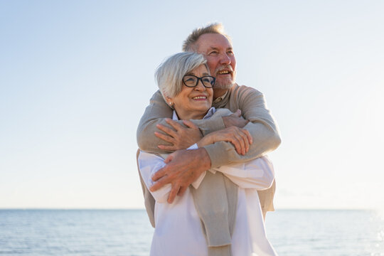 Senior mature couple hugging enjoying outdoor recreation walking on beach. Old husband wife embracing with tenderness love enjoying sweet bonding. Grandmother grandfather together. Family moment love
