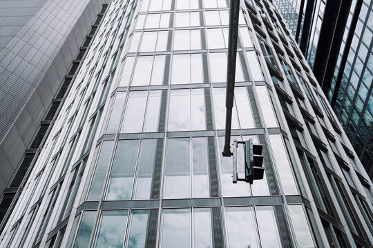 Glass facade of modern office skyscraper in Frankfurt financial area shot upward with traffic light emphasizing architecture lines and city scale