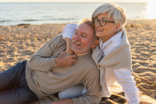 Senior mature couple sitting on beach hugging enjoying outdoor recreation. Old husband wife embracing with tenderness love enjoying sweet bonding. Grandmother grandfather together. Family moment love