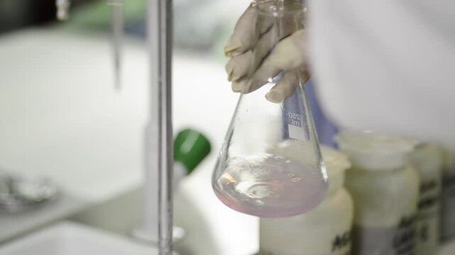 Scientist in protective gloves swirling chemical in glass flask