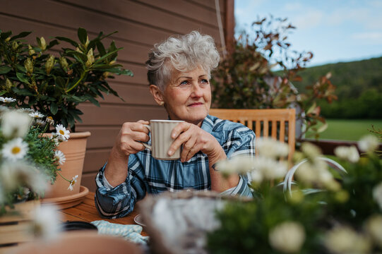 Senior woman with coffee sitting on terrace, resting after gardening.