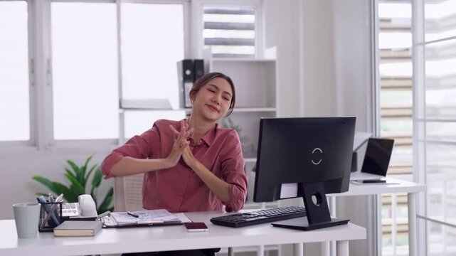 Asian adult woman office worker stretching arms above head enjoying a comfortable break at her modern workspace promoting healthy work habits and wellness
