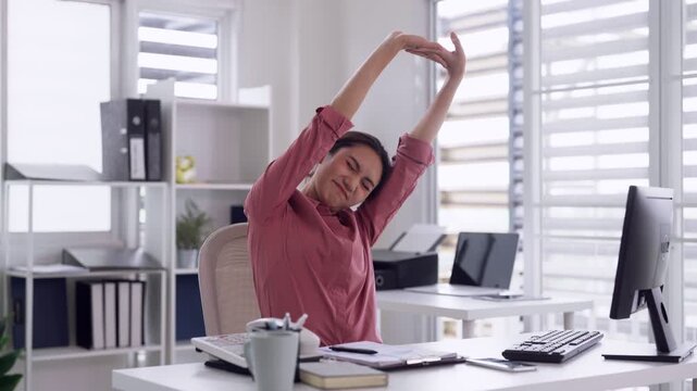 Asian adult woman office worker stretching arms relieving fatigue during long workday at modern desk home office workspace wellness break