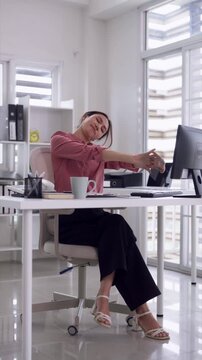 Adult Asian woman professional worker stretching arms taking break modern office workspace relieve work strain computer fatigue