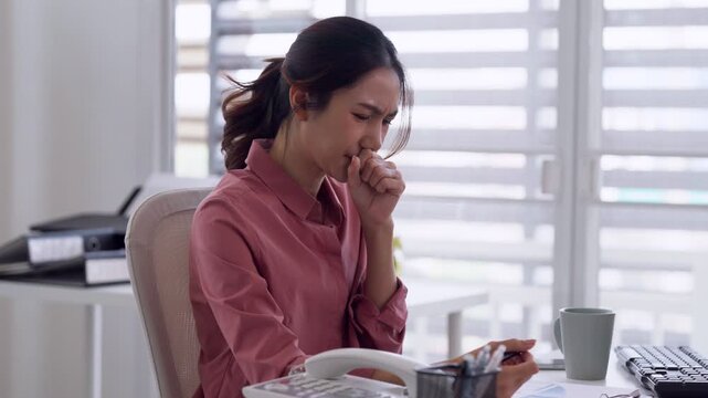 Asian adult woman coughing covering mouth feeling sick at home office desk working unwell employee health issue workplace illness concept