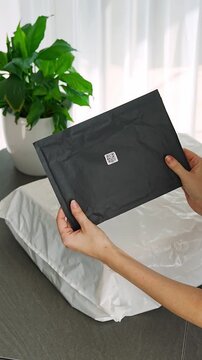 Person holding small parcel with compact QR code label compared to larger package at home. Different sizes of tracking codes for shipping and logistics concept.