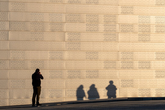 Urban pedestrian in Oslo Norway against wall texture with sunlight and shadow expressing minimalism and solitude in quiet street space
