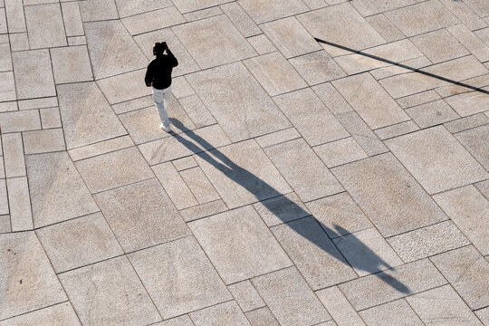 Overhead urban pedestrian casting shadow on Oslo Norway pavement pattern with geometry and minimalism in abstract city walkway design