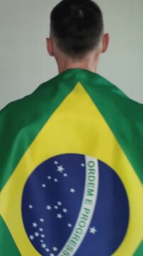 A man walks with a Brazilian flag over his shoulders, seen from behind. A football fan supporting his national team