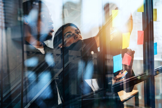 Team members collaborate at an office meeting while discussing ideas on a glass wall with colorful sticky notes in view
