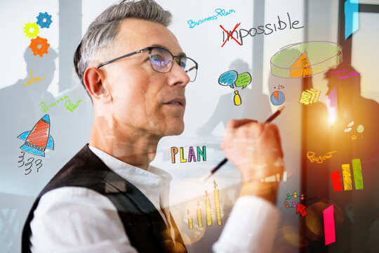 Business professional writing on glass with colorful drawings in a meeting room in the afternoon