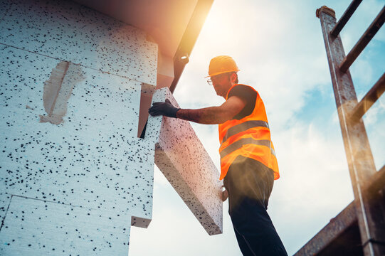 Worker installs building material on construction site during day near scaffold in bright sunlight