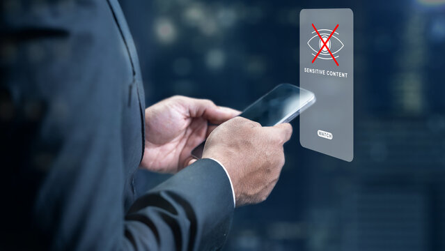 Professional man holding a smartphone with a digital holographic sensitive content warning icon, illustrating data privacy, internet safety, and content moderation policies
