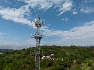 Obraz premium Communication base station tower on a rural hillside with green vegetation and village houses