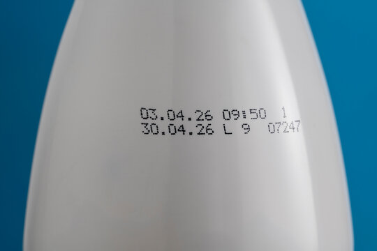 Expiration date printed on white bottle with dairy product. Closeup of manufacturing and expiry dates inkjetted on a white plastic bottle on blue background, focusing on product safety and shelf life