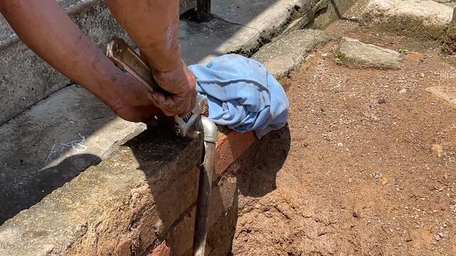 A man's hands using an adjustable wrench to rotate and tighten a metal pipe joint during a DIY home repair project outdoors.