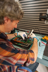 Fototapeta premium Man soldering electronic components on a laptop motherboard for repair and maintenance service